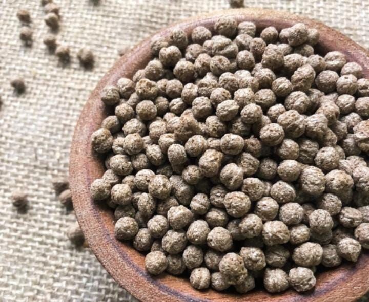 Bolitas de comida marrones y esféricas llenan un recipiente de madera y se derraman sobre una superficie de arpillera.