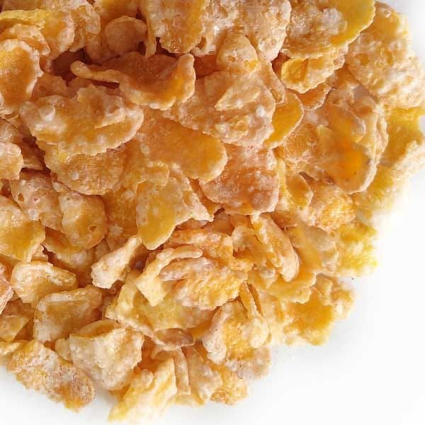 Primer plano de copos de maíz dorados, texturizados y ligeramente brillantes, en una pila sobre un fondo blanco.
