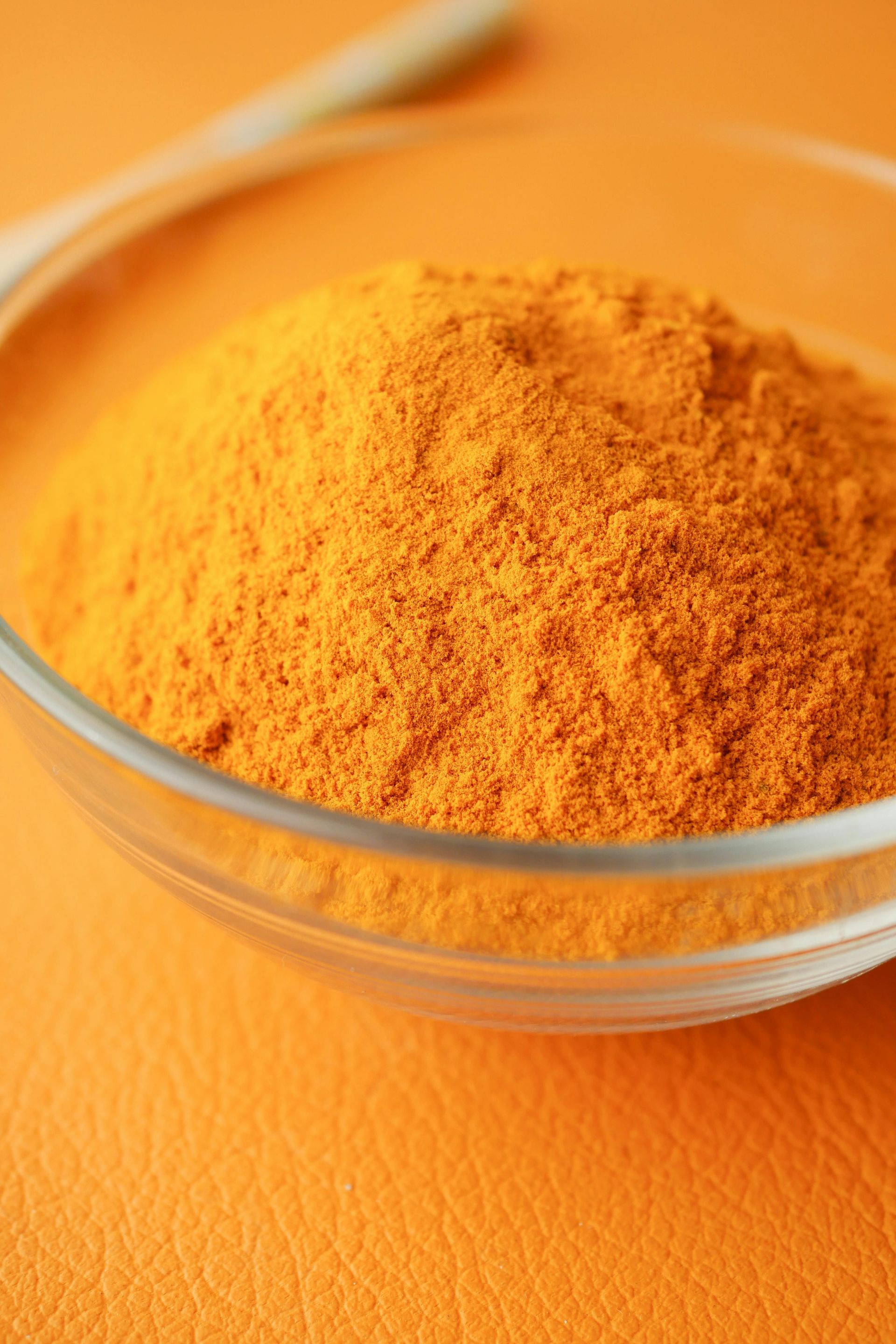 Polvo de cúrcuma en un recipiente de vidrio transparente sobre una superficie naranja.