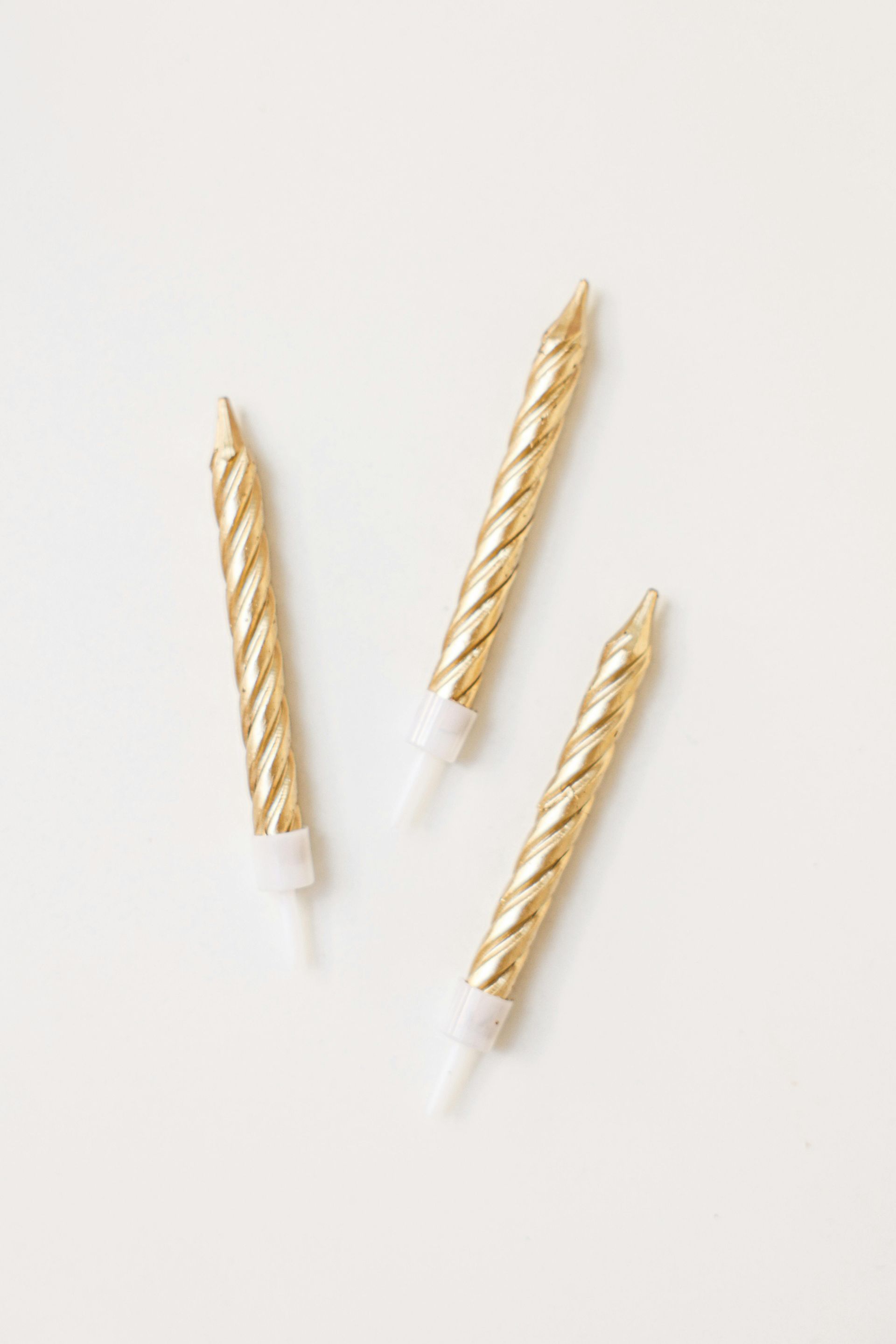 Tres velas de cumpleaños doradas sobre una superficie blanca.