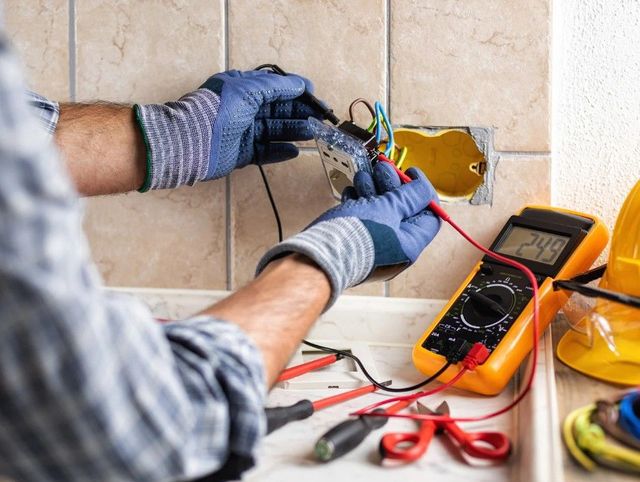 Elektriker prüft eine geöffnete Steckdose mit einem Messgerät