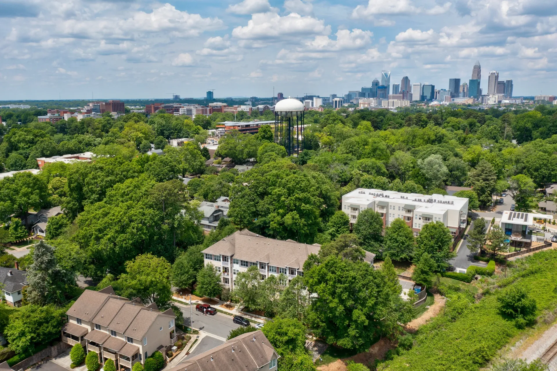 Aerial view of a green residential area with buildings and a skyline in the background.