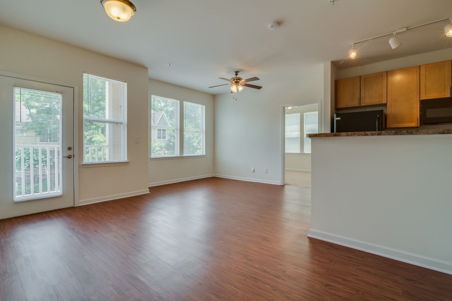 Spacious living area of an apartment with large windows and a ceiling fan.