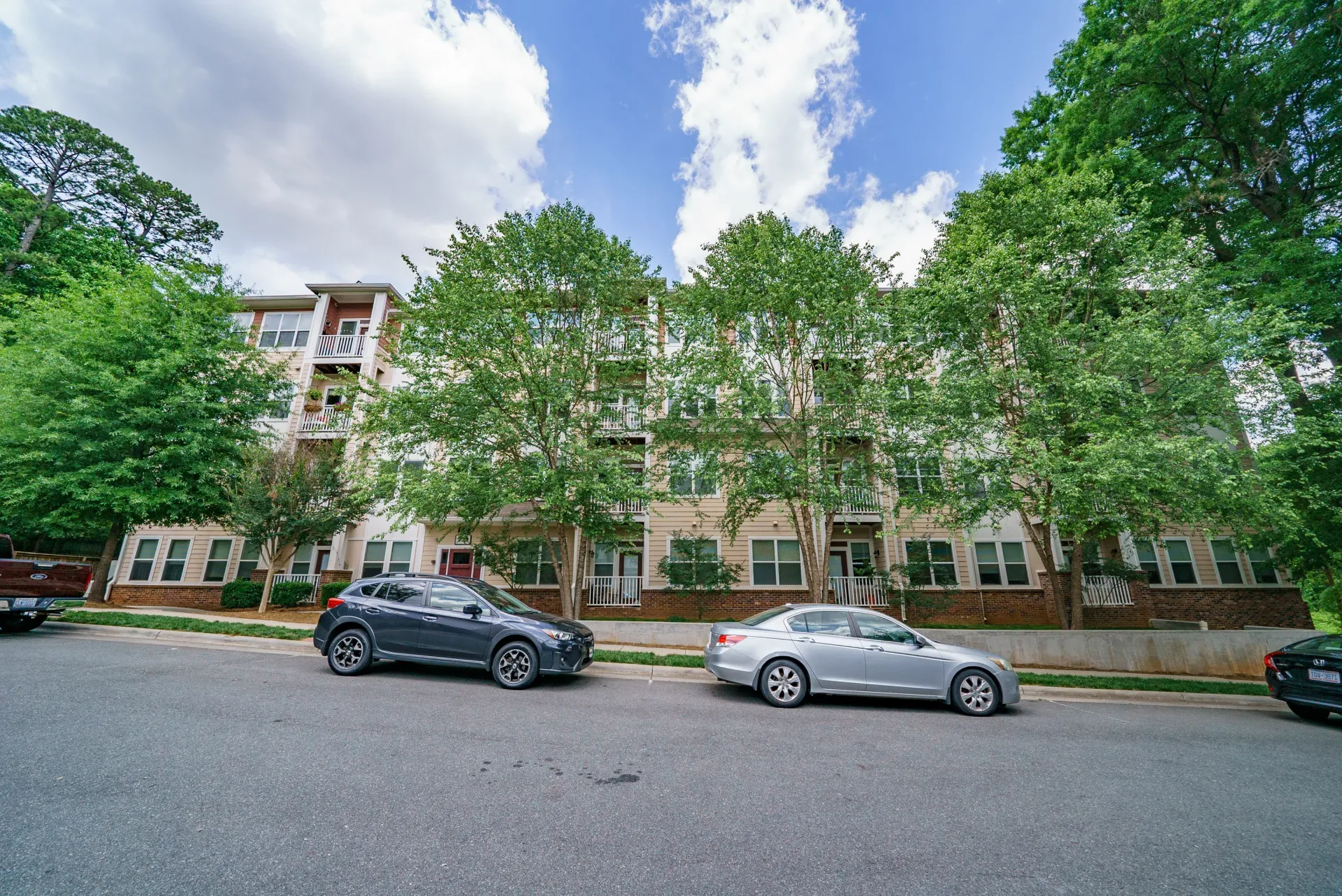 Exterior view of an apartment building with trees and parked cars