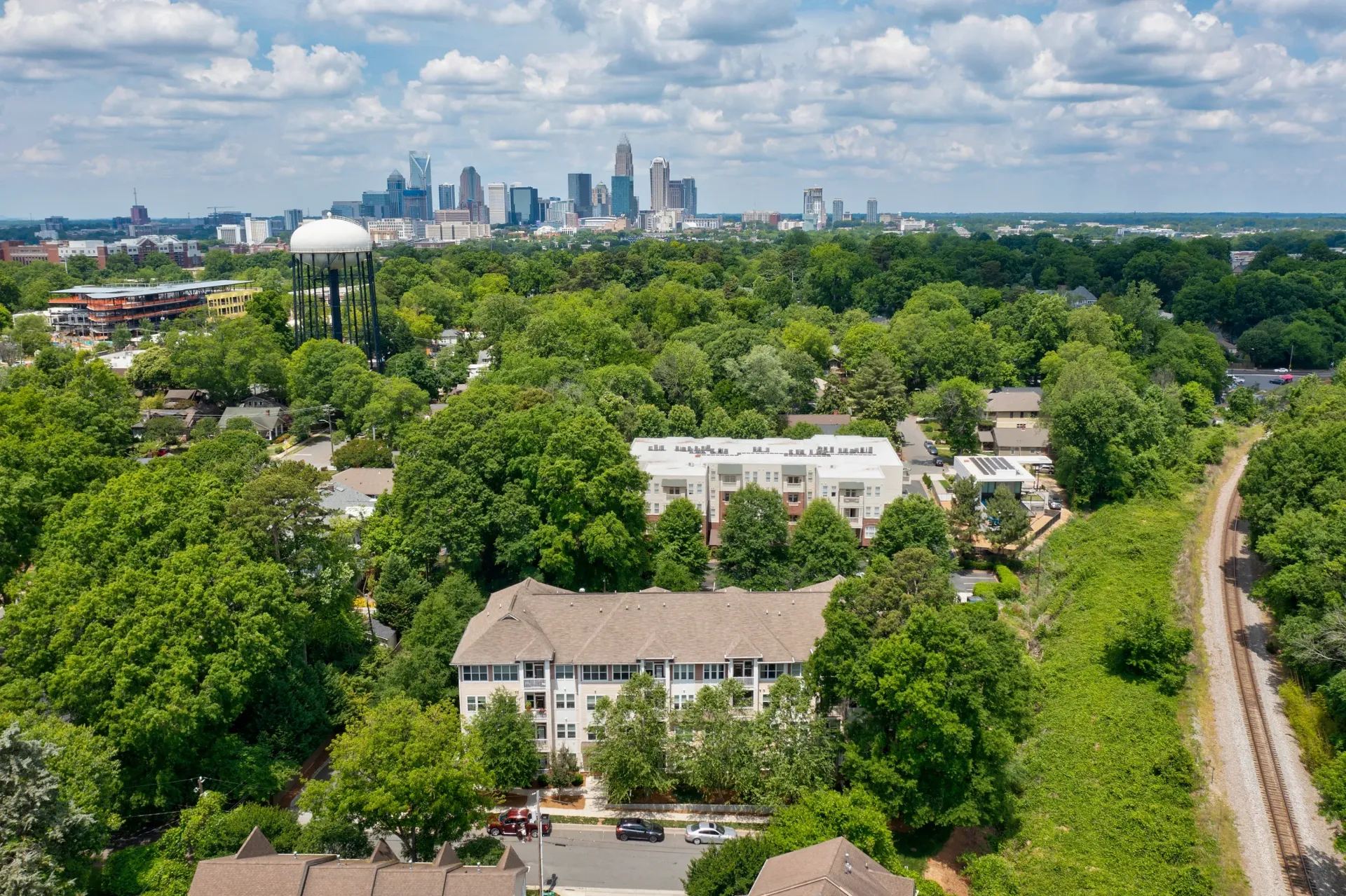 Aerial view of a residential community with buildings and greenery, city skyline in the background.