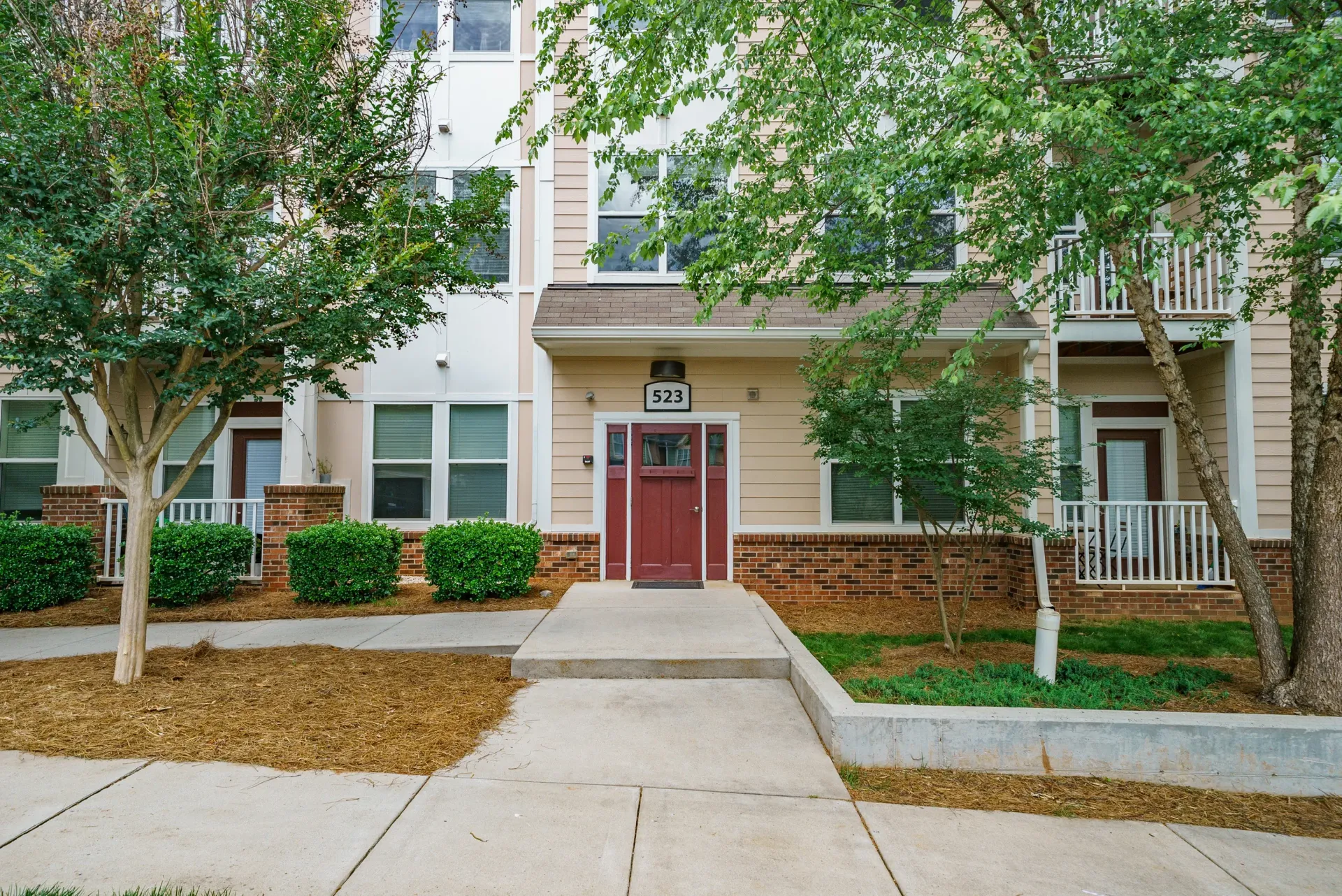 Exterior view of an apartment building entrance with a path and greenery.