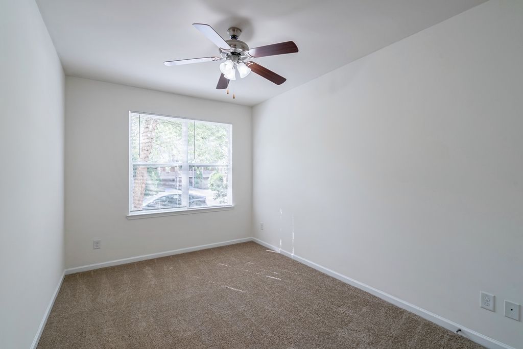 Interior view of a vacant apartment bedroom with a ceiling fan and window.