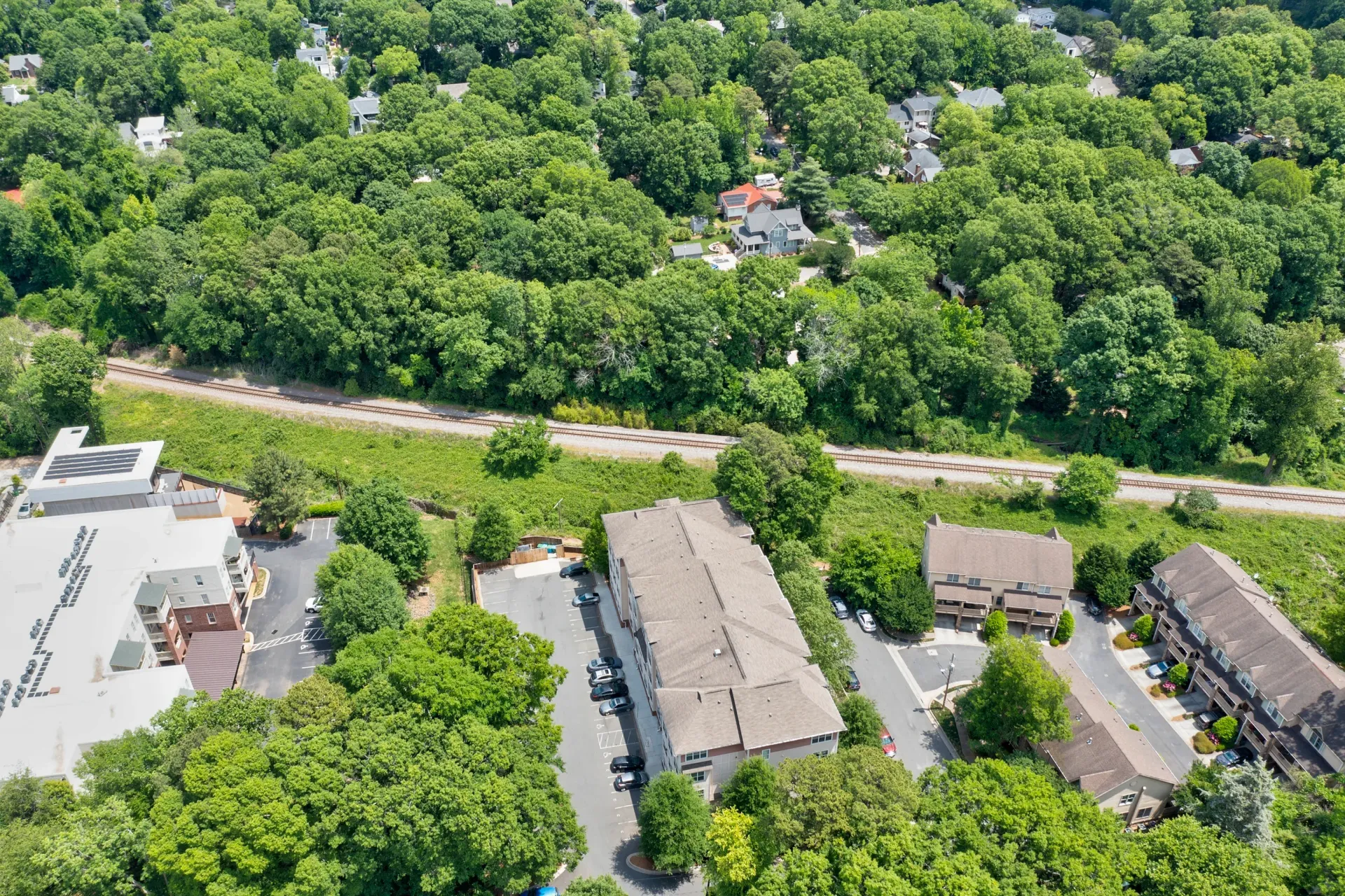 Aerial view of buildings surrounded by lush green trees, with a train track running through the center.