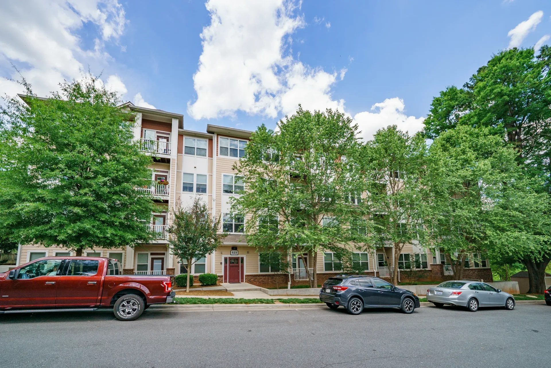 Exterior view of an apartment building with trees and parked cars