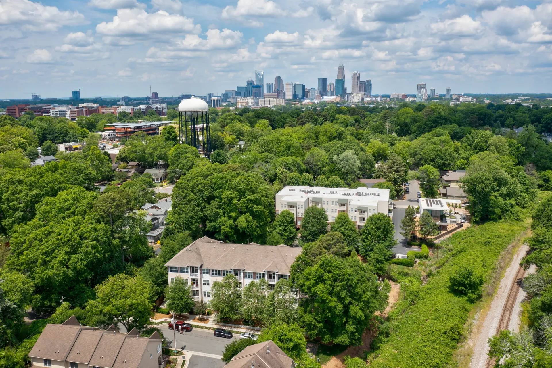 Aerial view of a residential community with greenery and a city skyline in the background.
