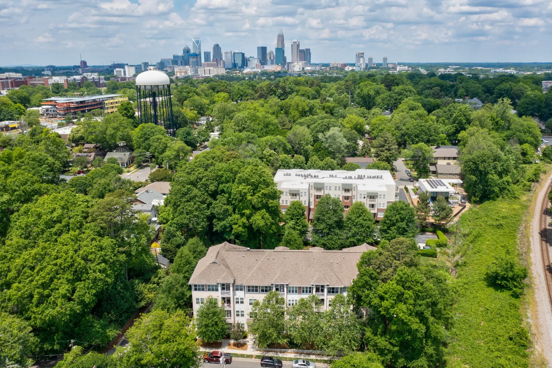 Aerial view of a residential community with greenery and city skyline in the background.