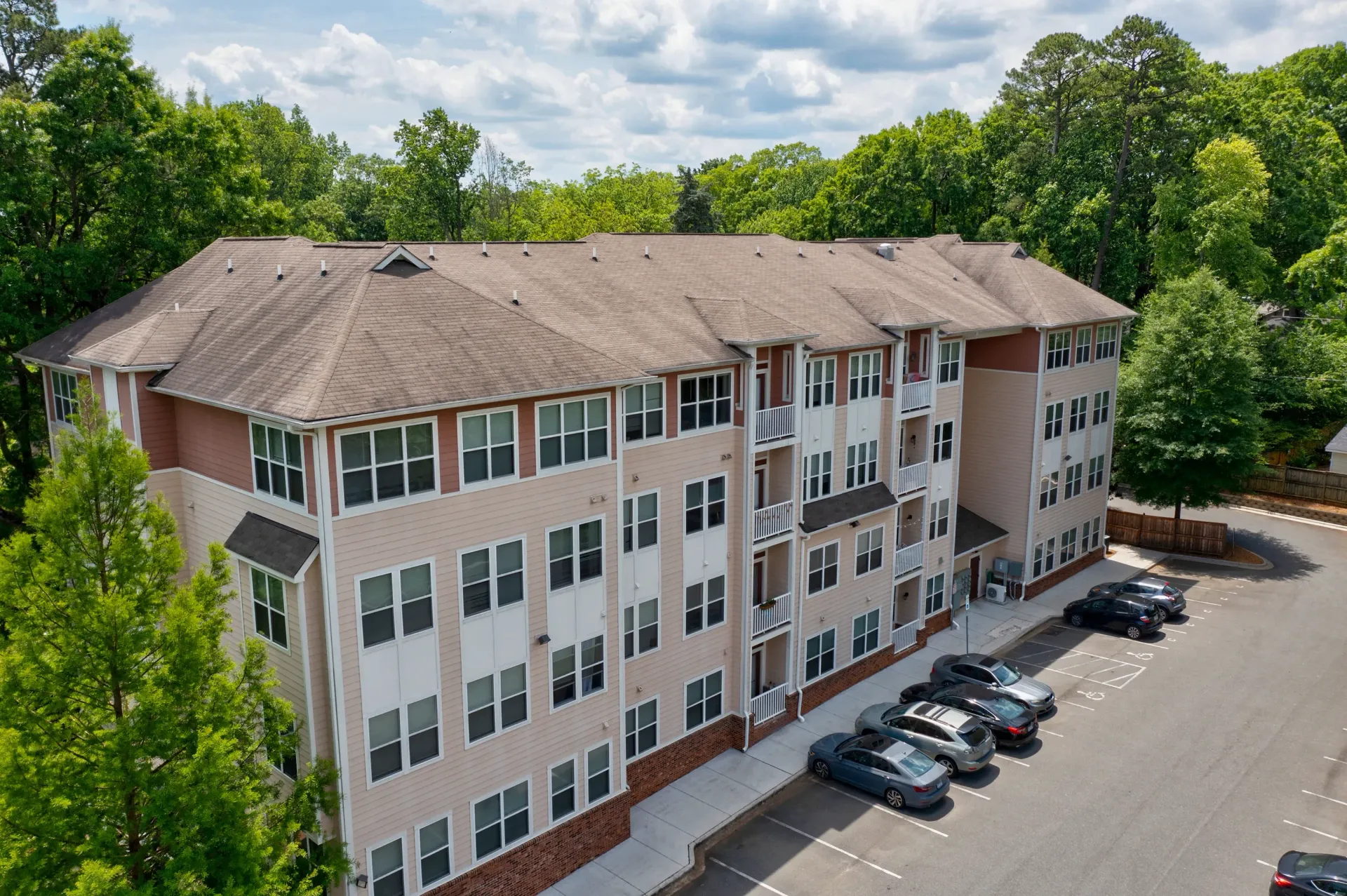 Exterior view of a multi-unit apartment building with surrounding greenery and parking area.