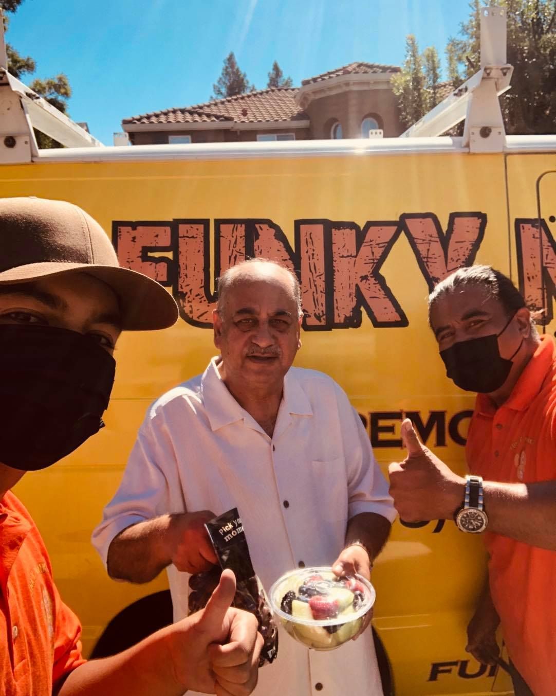 Three people with thumbs up, smiling, holding fruit in front of a yellow 