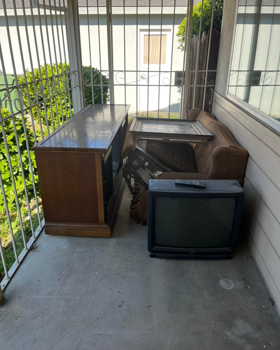 Porch with old TV, cabinet, and worn sofa behind a metal gate.