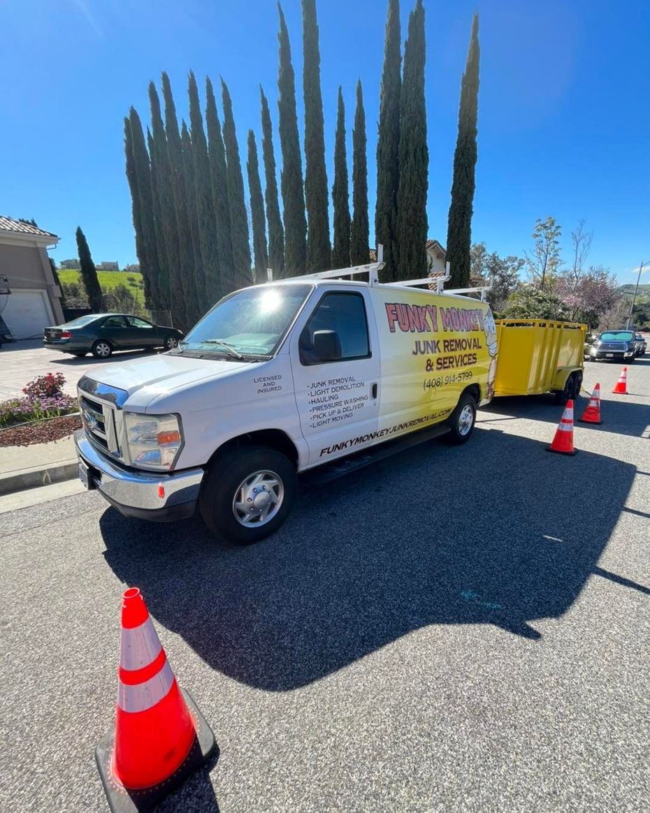 Funky Monkey junk removal truck parked on a lawn with a sign, white fence and cars in background.