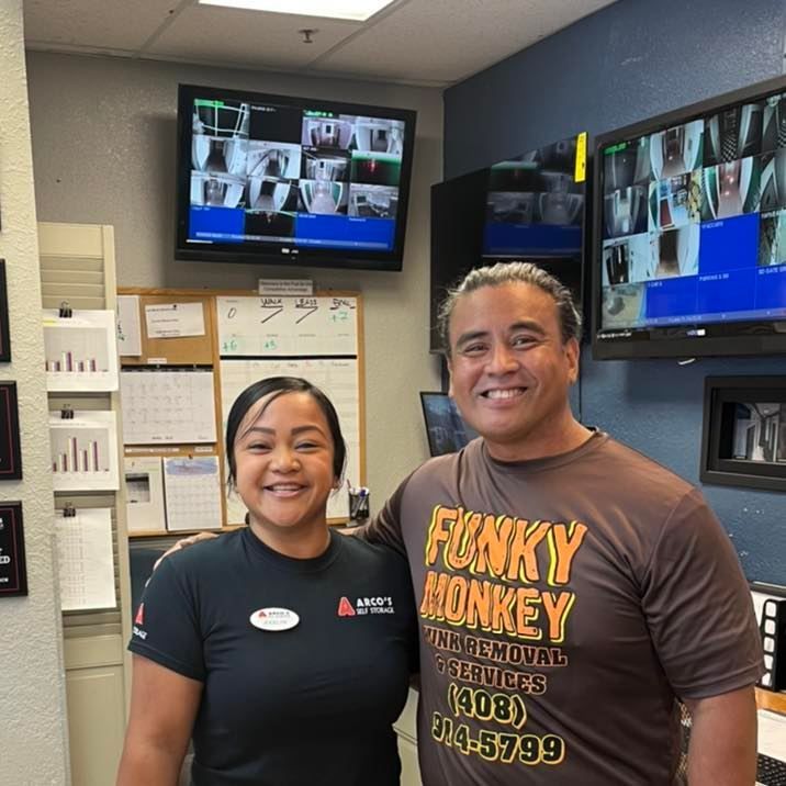 Two people smile in front of security monitors. 