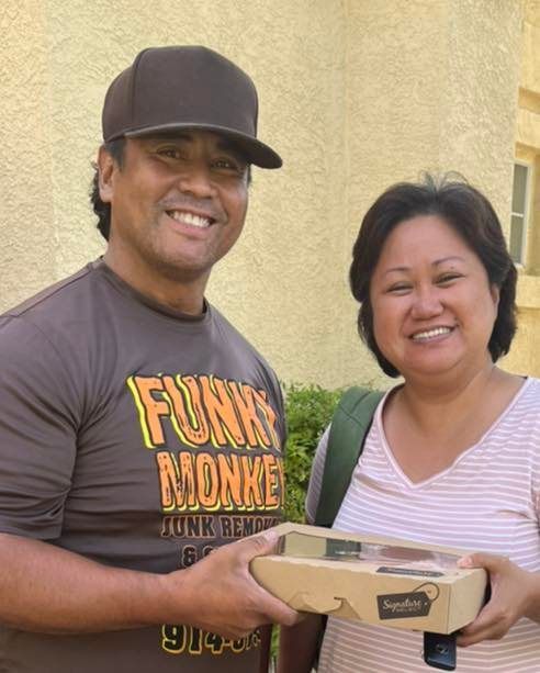 Man in brown hat and shirt and woman smile holding a box outdoors.