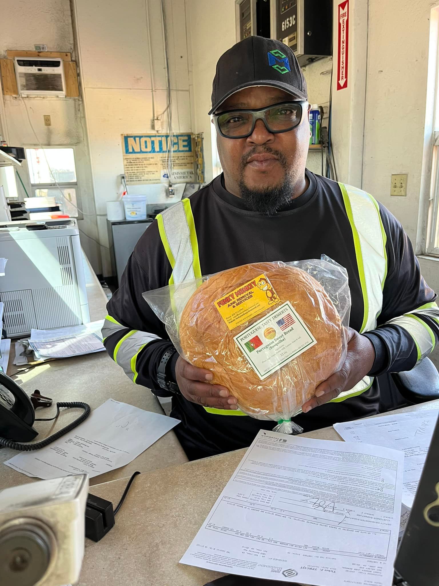 Man in reflective vest holding packaged bread at a desk with papers.