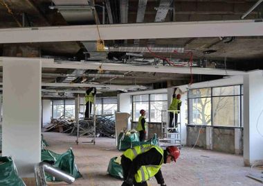 Construction workers in a building, wearing safety vests and hard hats, working on the ceiling.