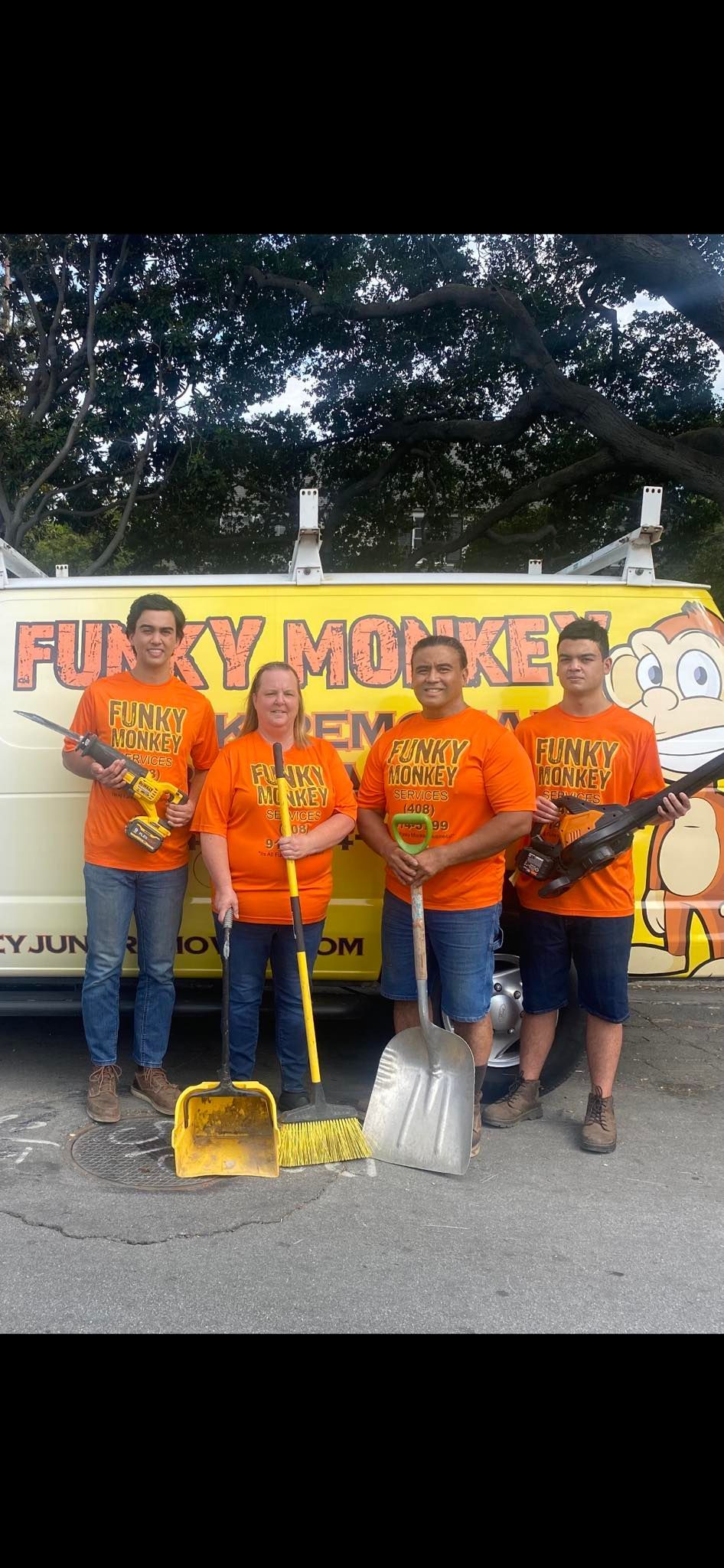 Four people in orange shirts stand in front of a yellow van, holding tools like shovels.