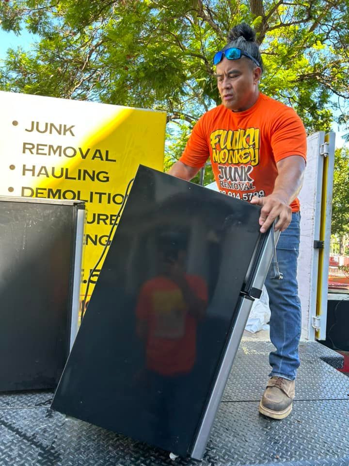 Man in orange shirt lifting a black appliance onto a truck for junk removal.