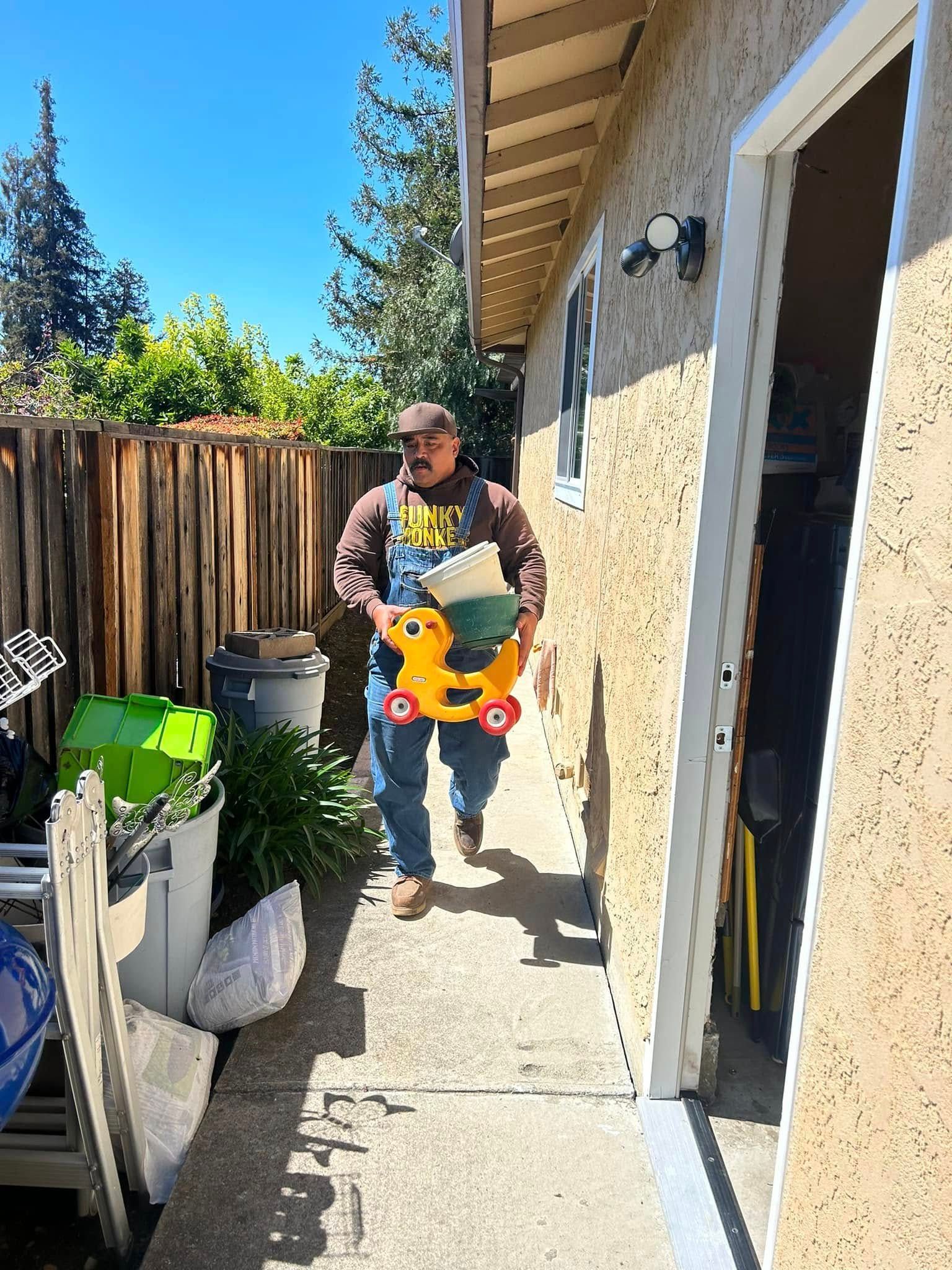 Man carrying a yellow toy duck walking along a concrete pathway next to a building on a sunny day.
