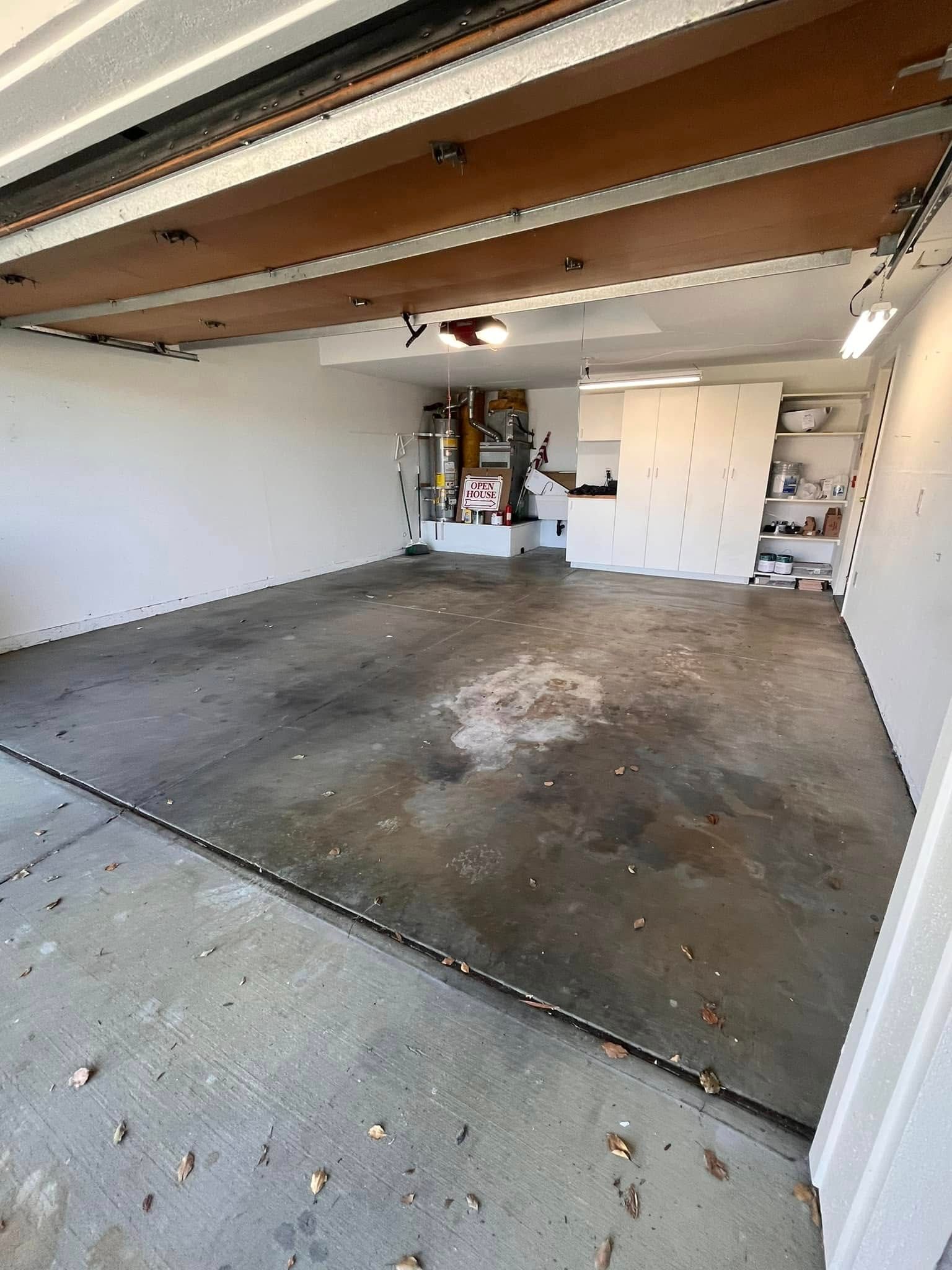 Empty garage with dirty concrete floor, white walls, and overhead garage door.