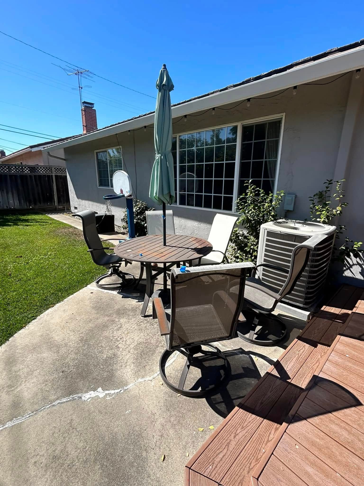 Patio with table, chairs, umbrella, and air conditioner next to a house under a clear sky.