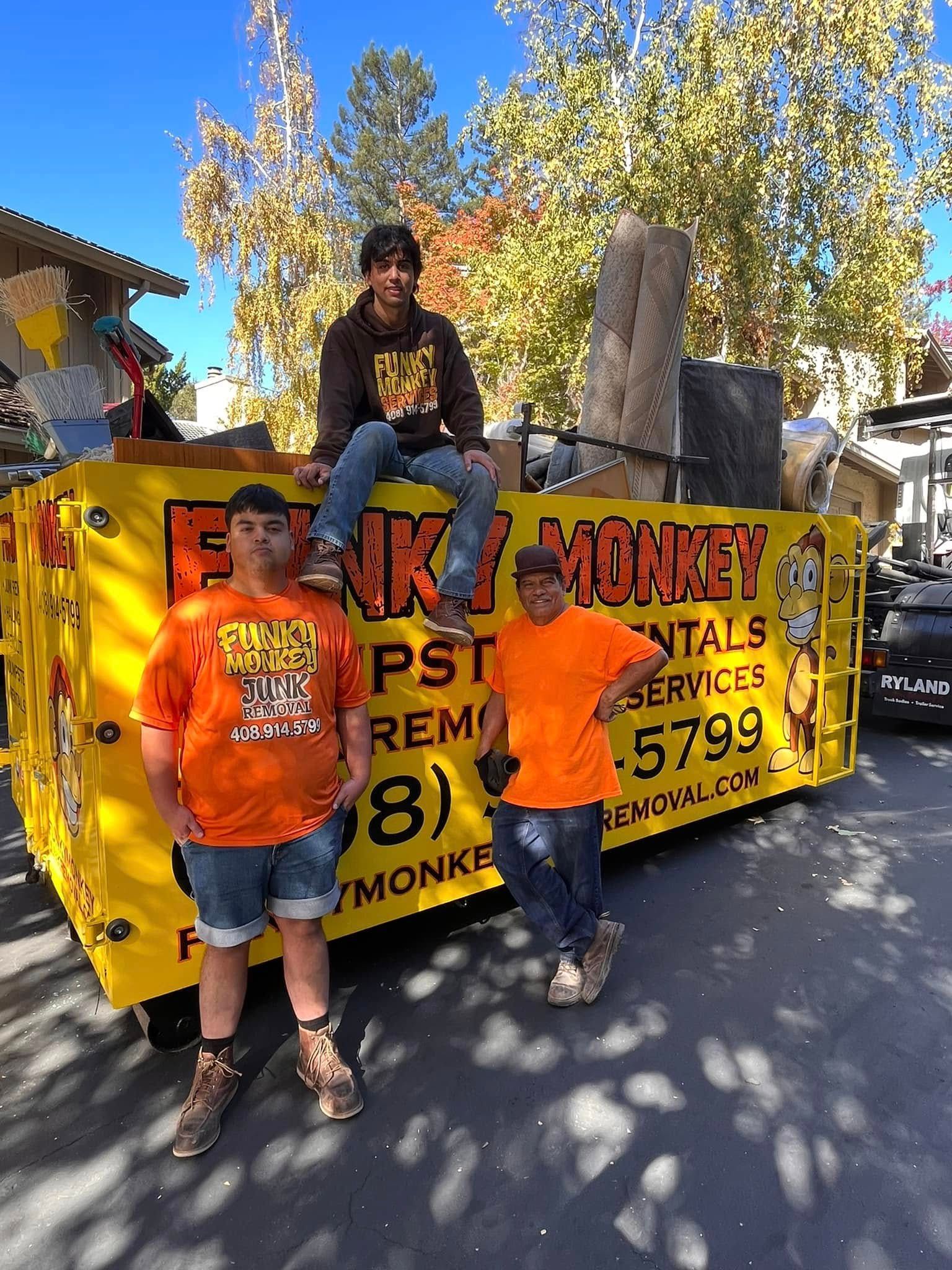 Three people in front of a yellow dumpster with 