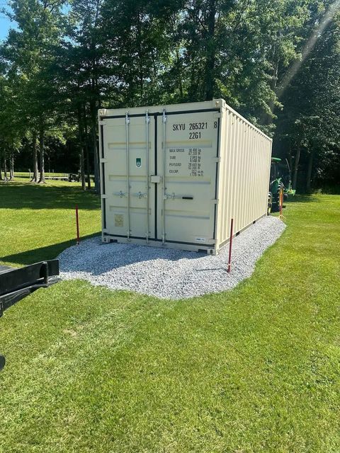 A shipping container is sitting in the middle of a grassy field.