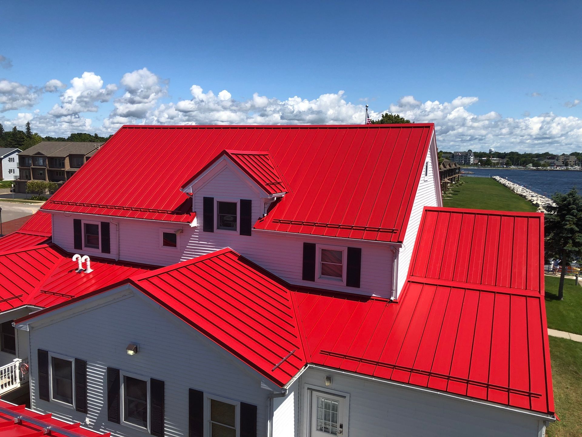 Drone shot of the Ludington Coast Guard building, showcasing a vibrant Regal Red standing seam metal roof by Riegle Metals. The aerial perspective highlights the bold color and seamless installation, enhancing the building's coastal resilience and striking design.