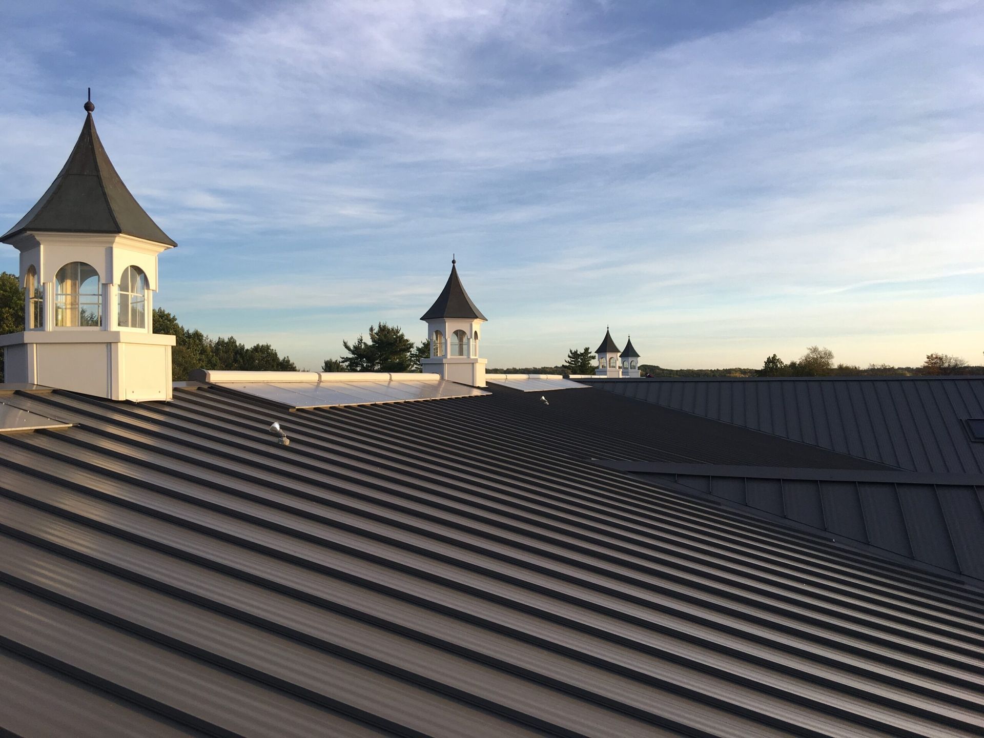 Roof-level shot of a horse arena in Metamora, Michigan, featuring a Burnished Slate standing seam metal roof by Riegle Metals. The image captures the roof's smooth, precision-crafted panels, showcasing its durability and elegant finish against the structure.
