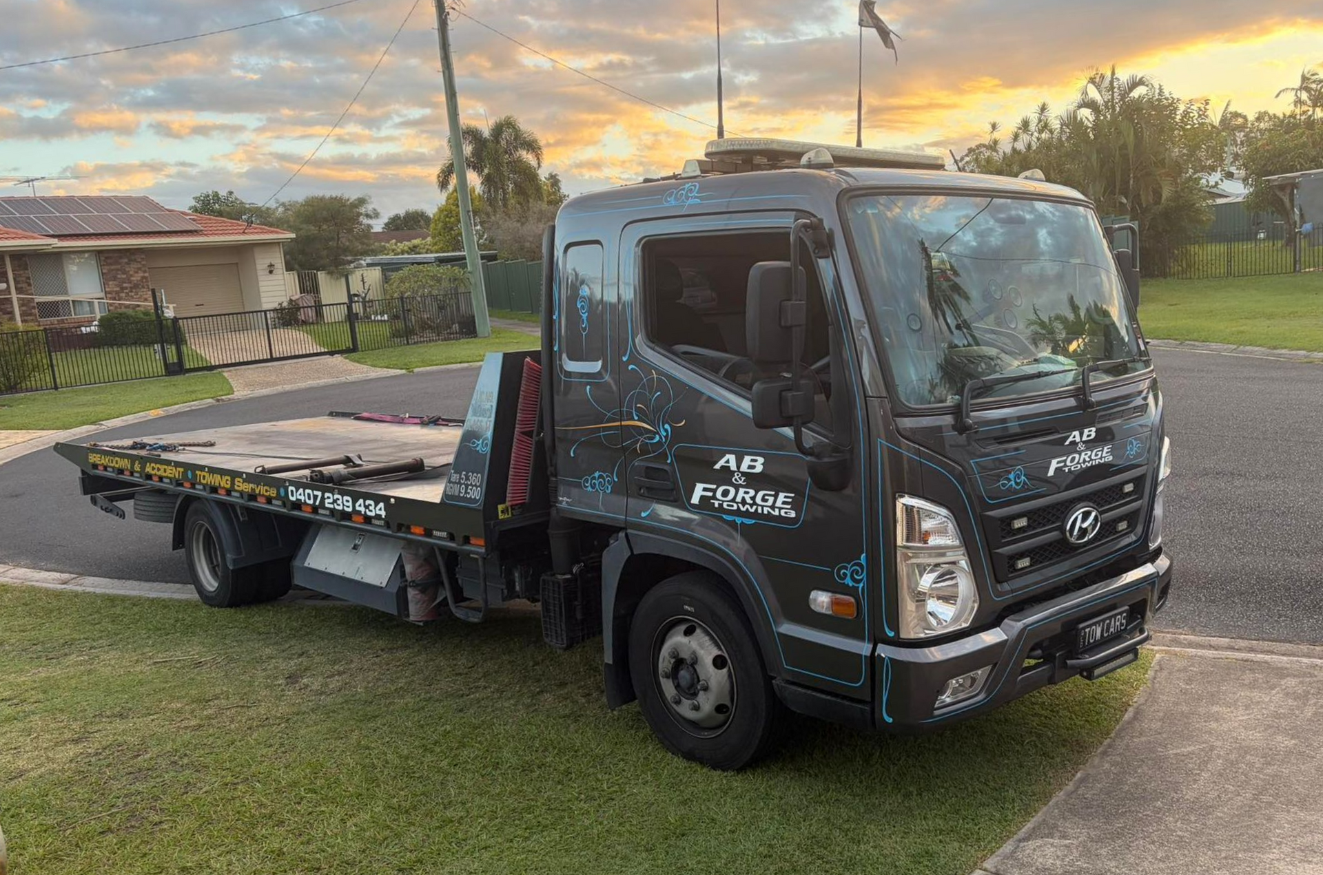 Black flatbed tow truck parked on grass at sunset — A B & Forge Towing In Caboolture, QLD