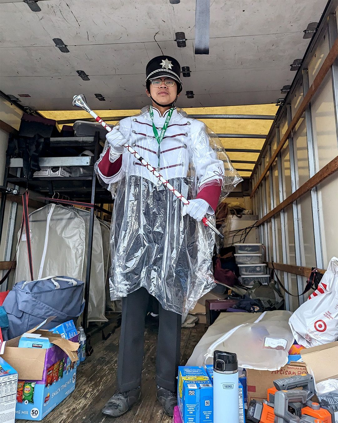 A man in a marching band uniform is standing in the back of a truck holding a cane.