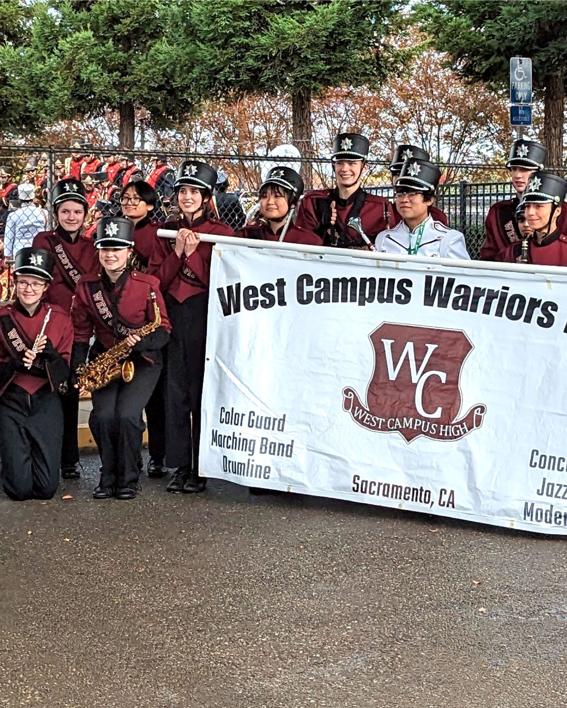 The West Campus Warriors marching band is posing for a picture with a banner.