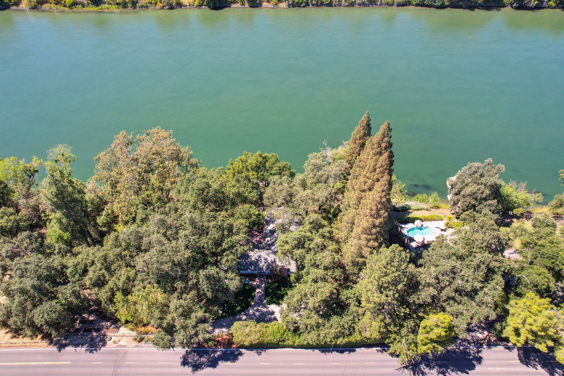 A peaceful riverside home surrounded by lush trees, with a private pool and easy road access for quiet waterfront living.