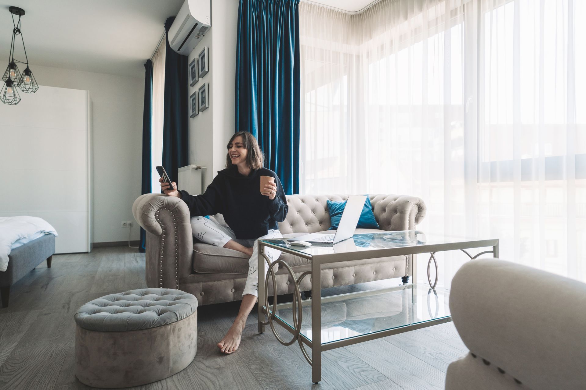 A woman sitting on a couch in a living room holding a cup of coffee and a phone