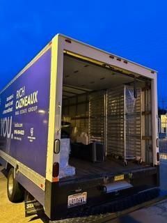 A blue and white truck with the back door open is parked on the side of the road.