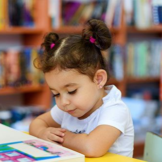 Girl with two top knots intently reads a book in a library.