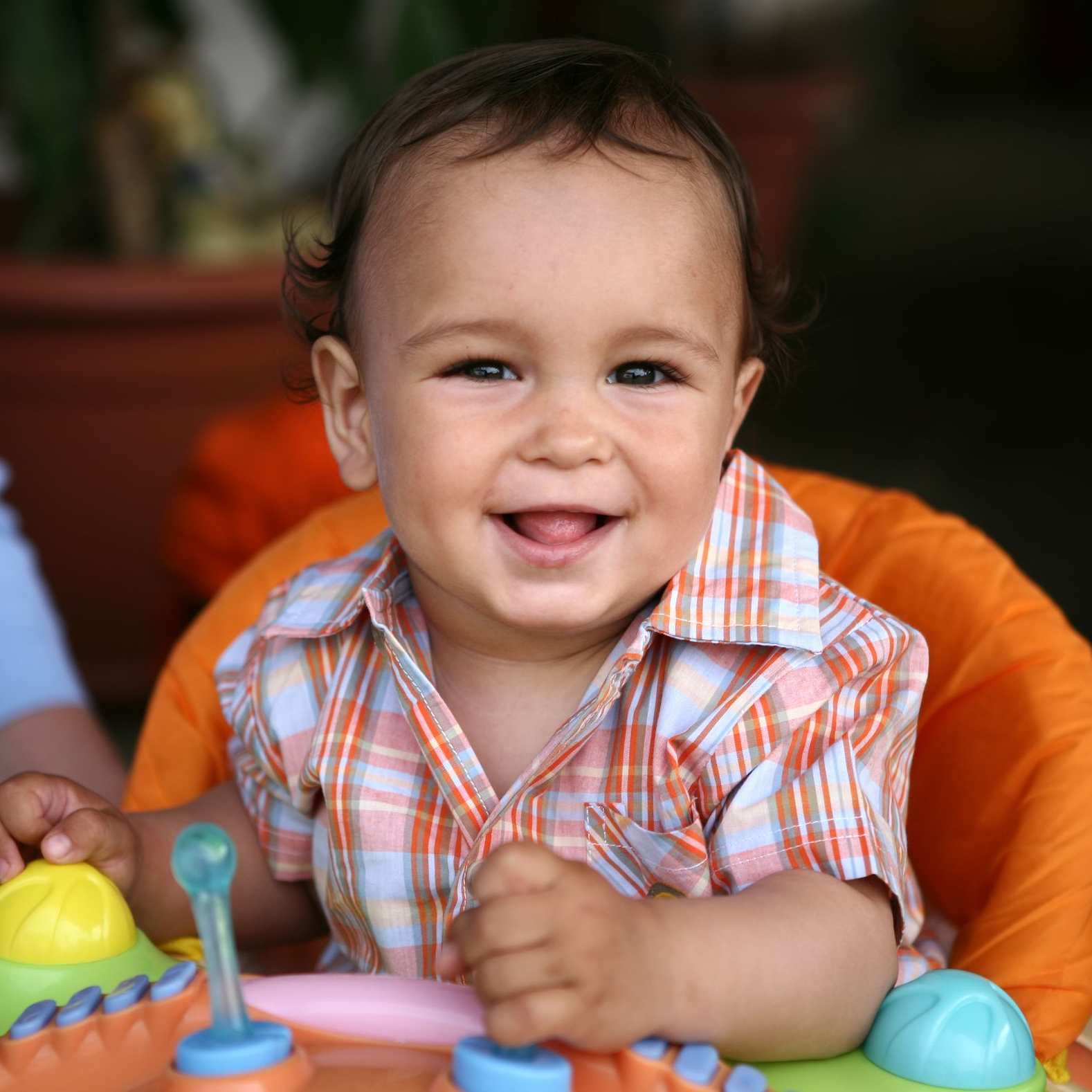 Smiling baby in an orange high chair wearing a plaid shirt.