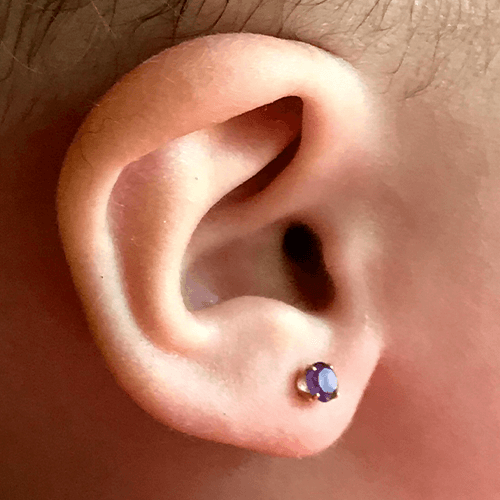 Close-up of a human ear with a small, round purple stud earring.