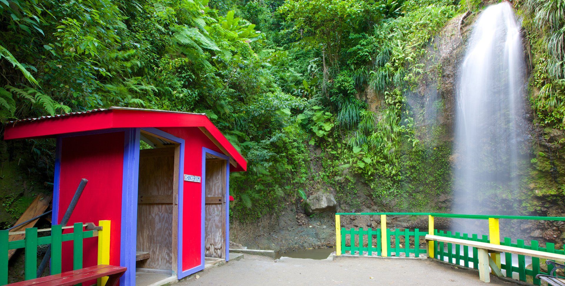 Waterfall behind brightly coloured yellow and green fence and Purple and Red hut