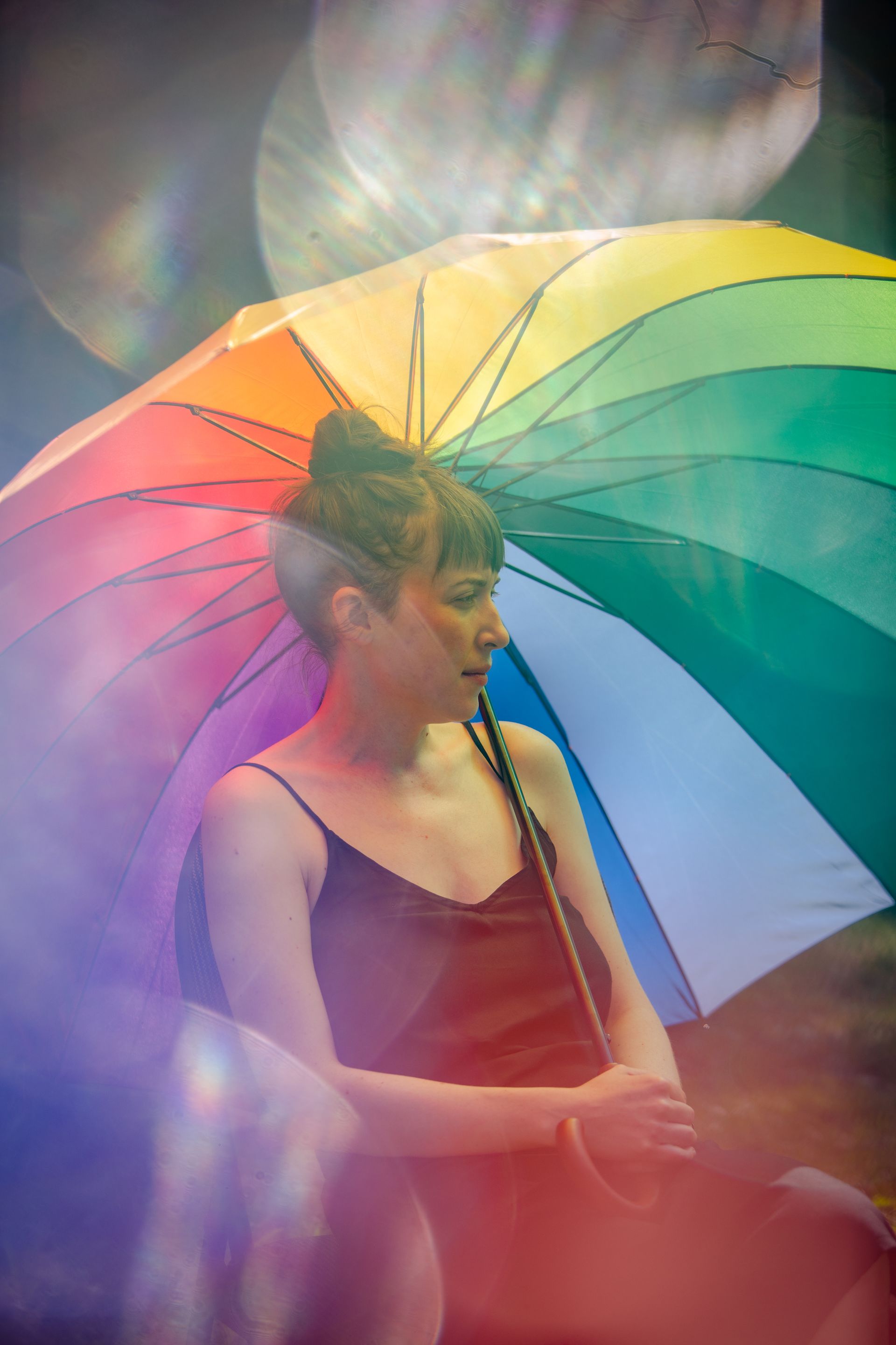 A person is sitting under a rainbow coloured umbrella.