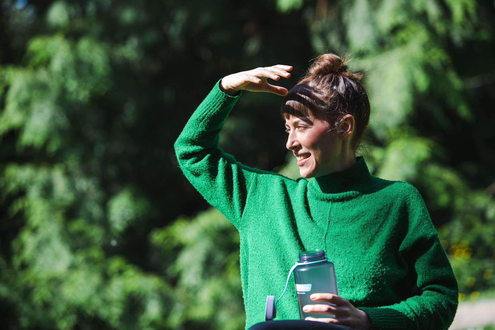 A person in a green sweater is holding a water bottle.