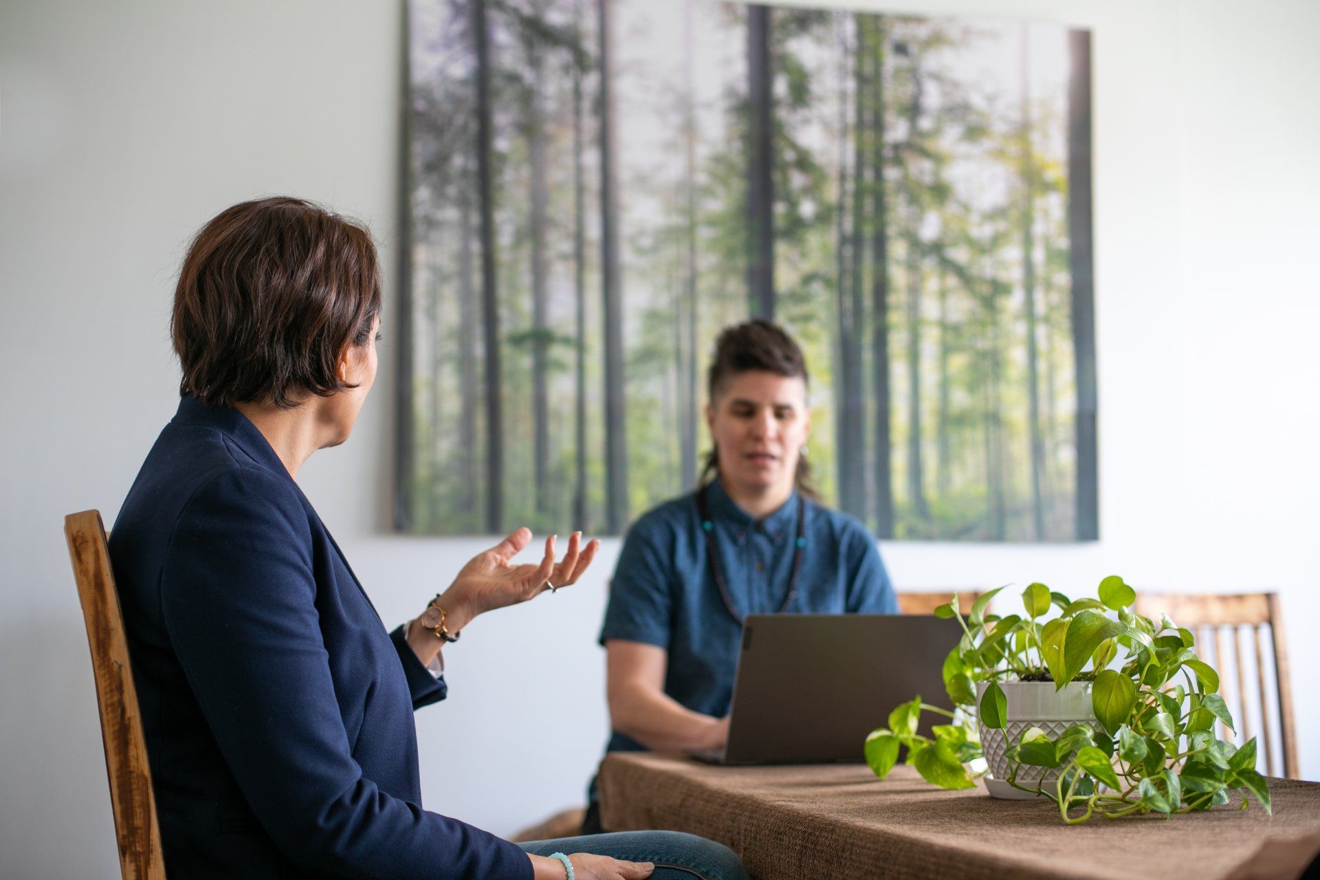 Two individuals are sitting at a table with a laptop.