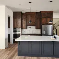 A kitchen featuring dark wood upper cabinets, a light-colored tile backsplash, and a large dark gray island with white top.
