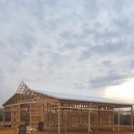 The wooden frame and white roof of a large building under construction set against a cloudy, sunset sky.