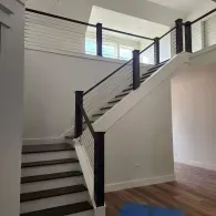 A staircase with dark wood treads and a cable railing system, set against white walls in a modern interior.