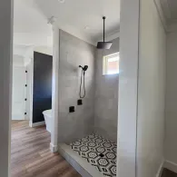 A modern shower with geometric patterned tile flooring, light gray subway tile walls, and matte black fixtures.