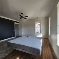 An empty mattress on a frame sits in a bedroom with white walls, a black accent wall, and light-colored wood flooring.